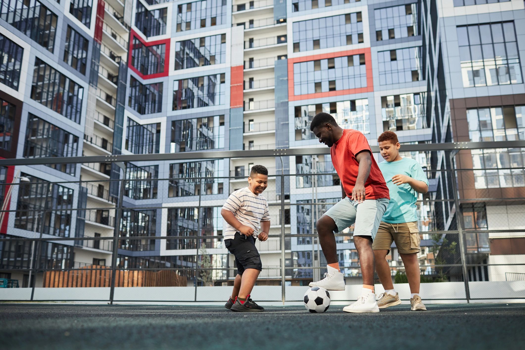 Coach playing soccer with youth outside a community building